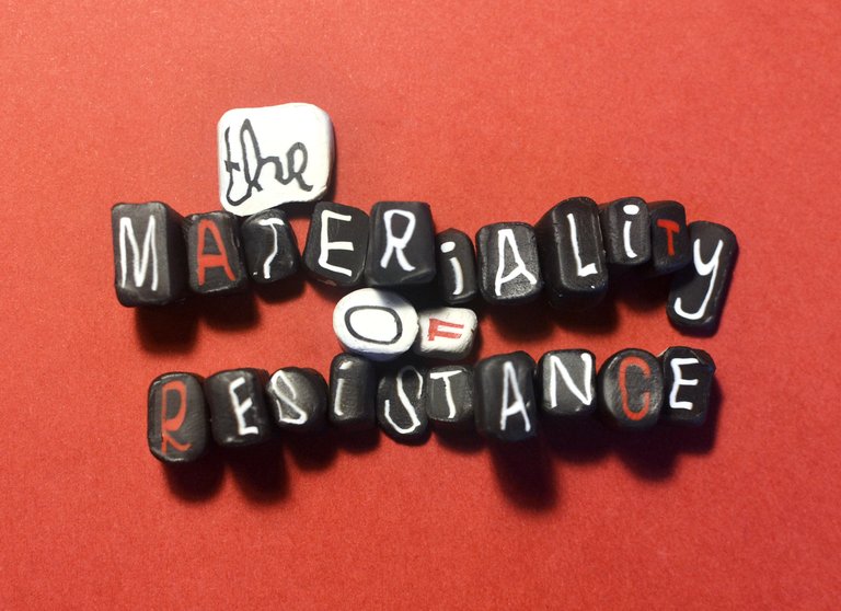Hand-shaped black and white clay murrini pieces with letters inside them, laid out to spell "The Materiality of Resistance."