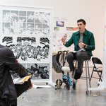 A design workshop in progress, led by a man wearing a green jacket.