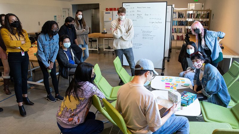 A group of twelve students gather in a circle around a table with post-its.