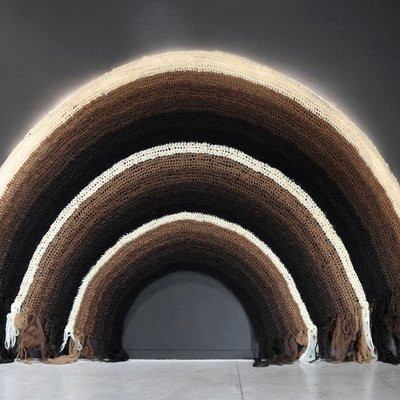 Photo of an artwork of a woven rainbow with bands of different rich hues of brown, blacks, and beige.