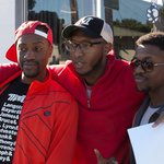 Three men stand side-by-side smiling at another camera out of view. Shane Watson is in the middle with his arms wrapped around their shoulders.
