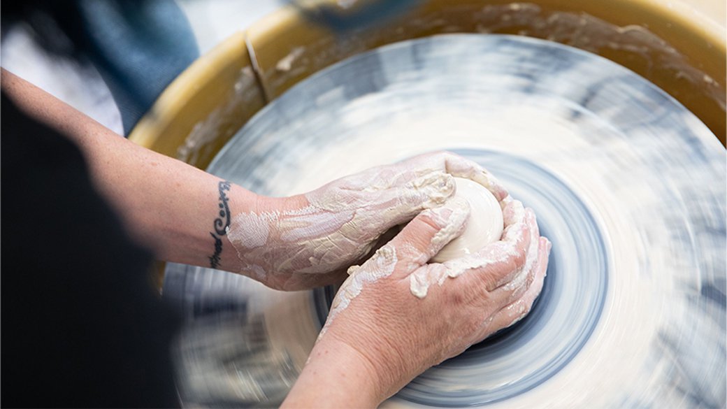 Close-up of hands forming a lump of white clay on a potter’s wheel in California College of the Arts’ ceramics studio.