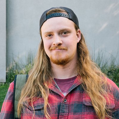 A man poses for the camera wearing a baseball hat backwards and a flannel shirt.