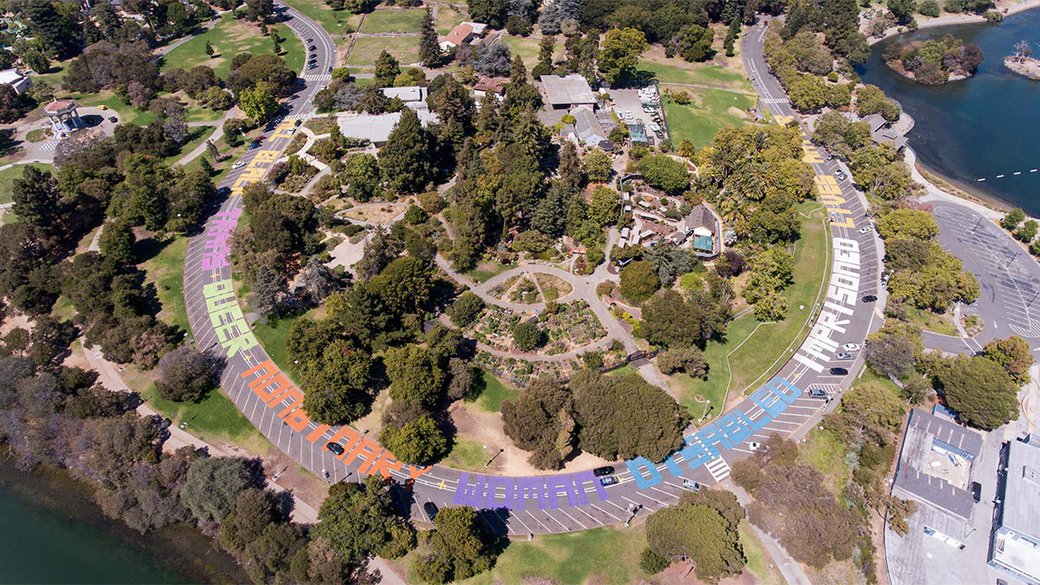 Drone view of The Gardens at Lake Merrit, the words, "All black trans queer nonbinary women's disabled imprisoned lives matter" are painted on the street.