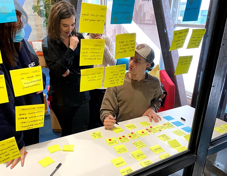 Eva Xu, Olive Brown, and Ryan Koble viewing yellow post-it notes on a glass wall at Google.