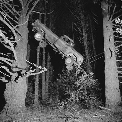 A black and white photograph of a car hanging from two trees.