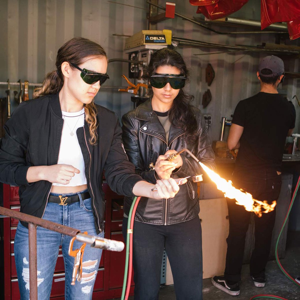 One student holds a torch, while another student ignites the flame.