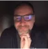 Person with glasses and beard resting chin on hand, looking at the camera