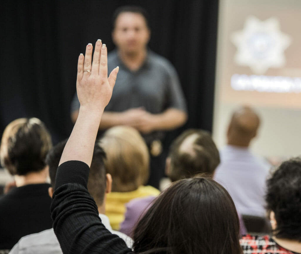 A woman raises her hand to ask Jacinto Rivera, an officer with Metropolitan Police Department Office of Community Engagement, a question during an immigration outreach enforcement meeting at East Las Vegas Community Center