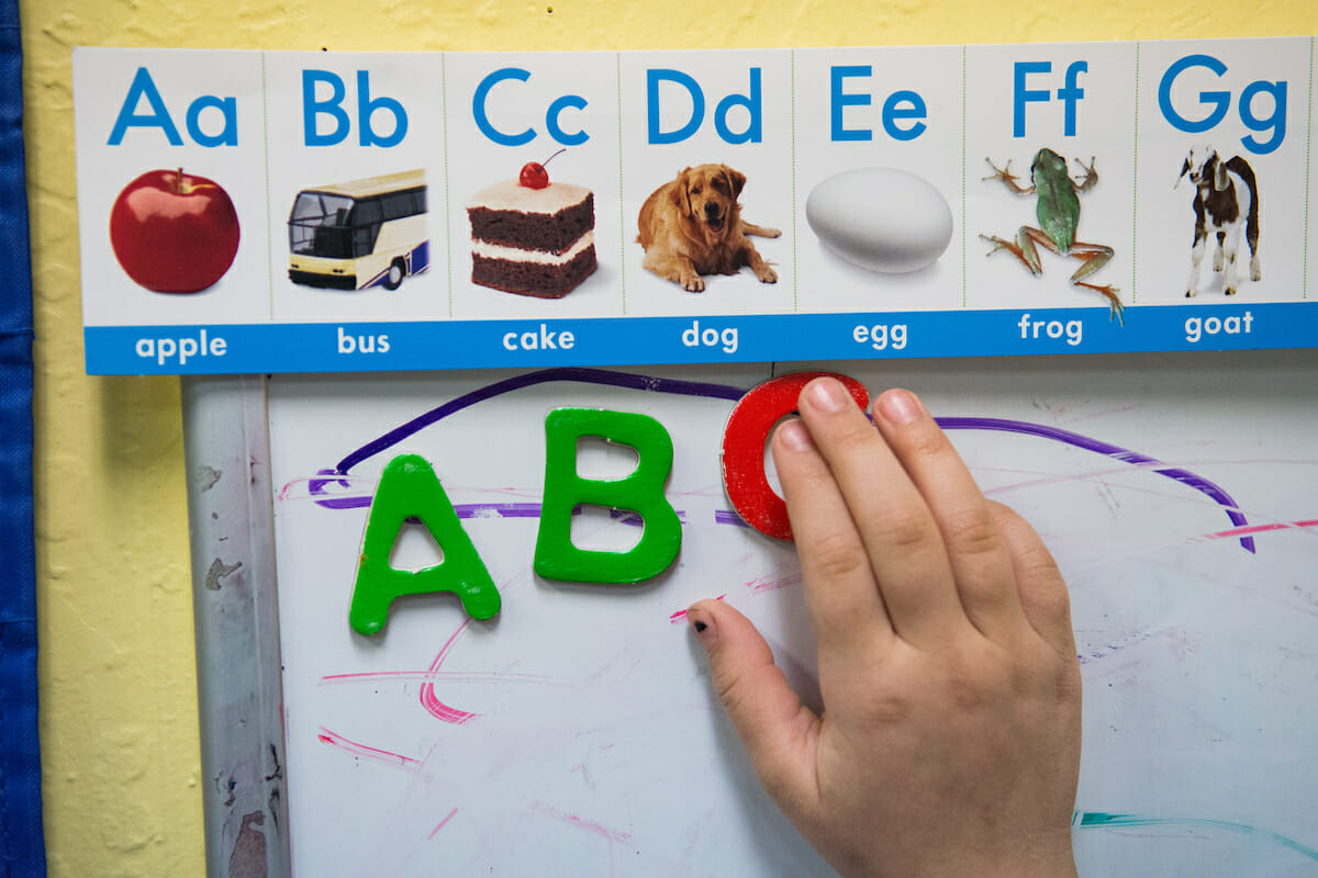 A magnetic white board with the letters a, b, and c being moved slightly by a hand