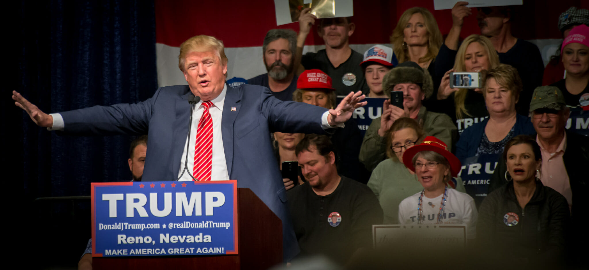 Then-candidate Donald Trump at the podium in a blue jacket and red tie.