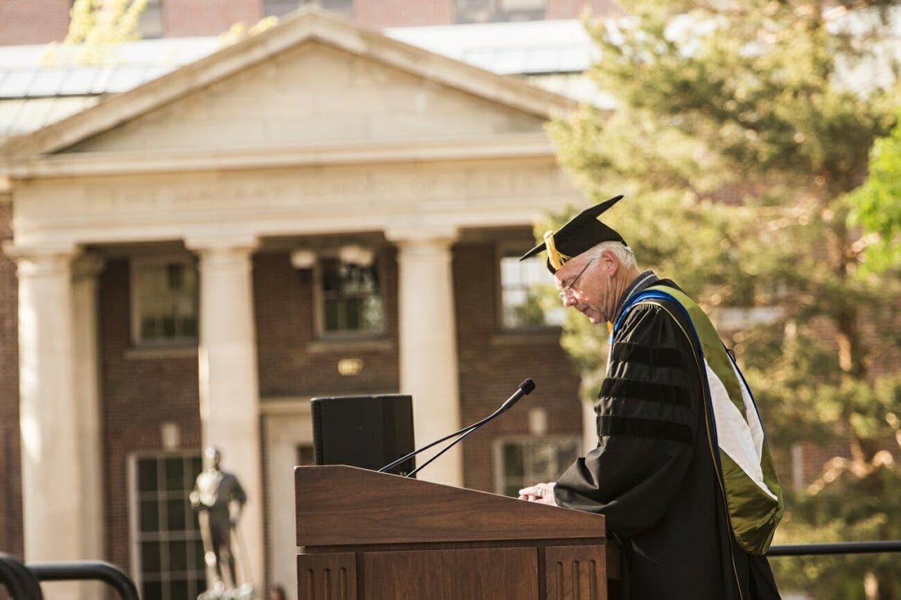 University of Reno president Marc Johnson speaking at a podium in cap and gown