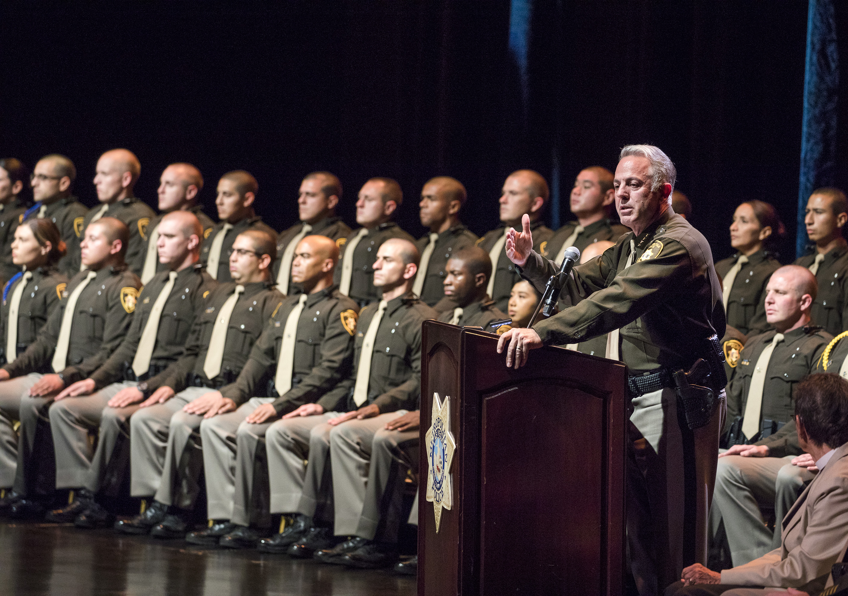 A group of recently graduated police officer sits on stage.