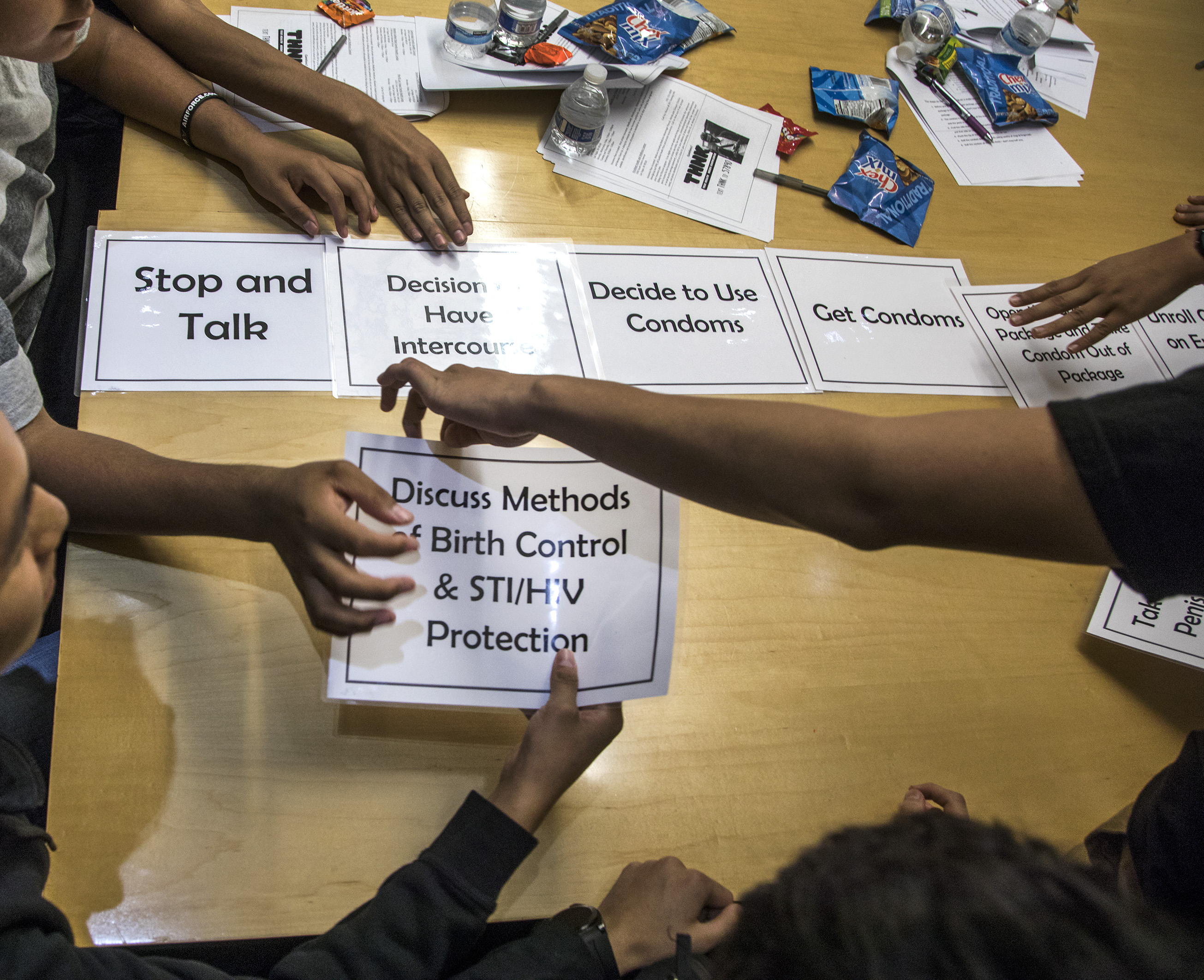 About five students with only arms showing, reaching into the center of a table