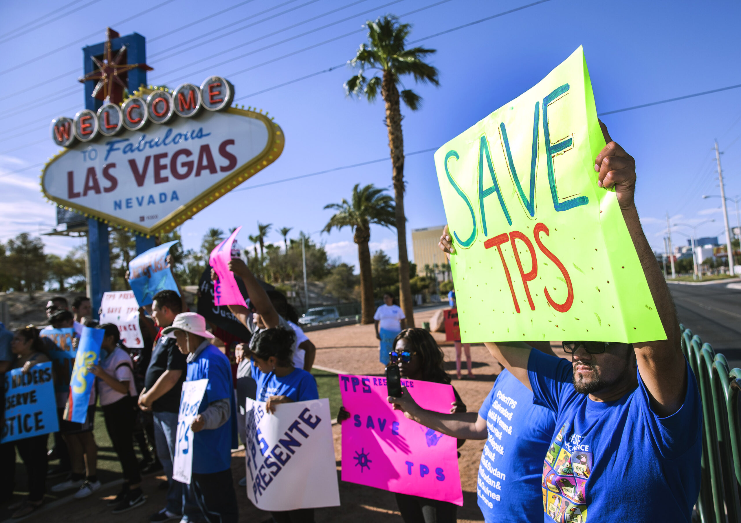 Protester holding a sign saying "save TPS" in front of the Welcome to Las Vegas Sign