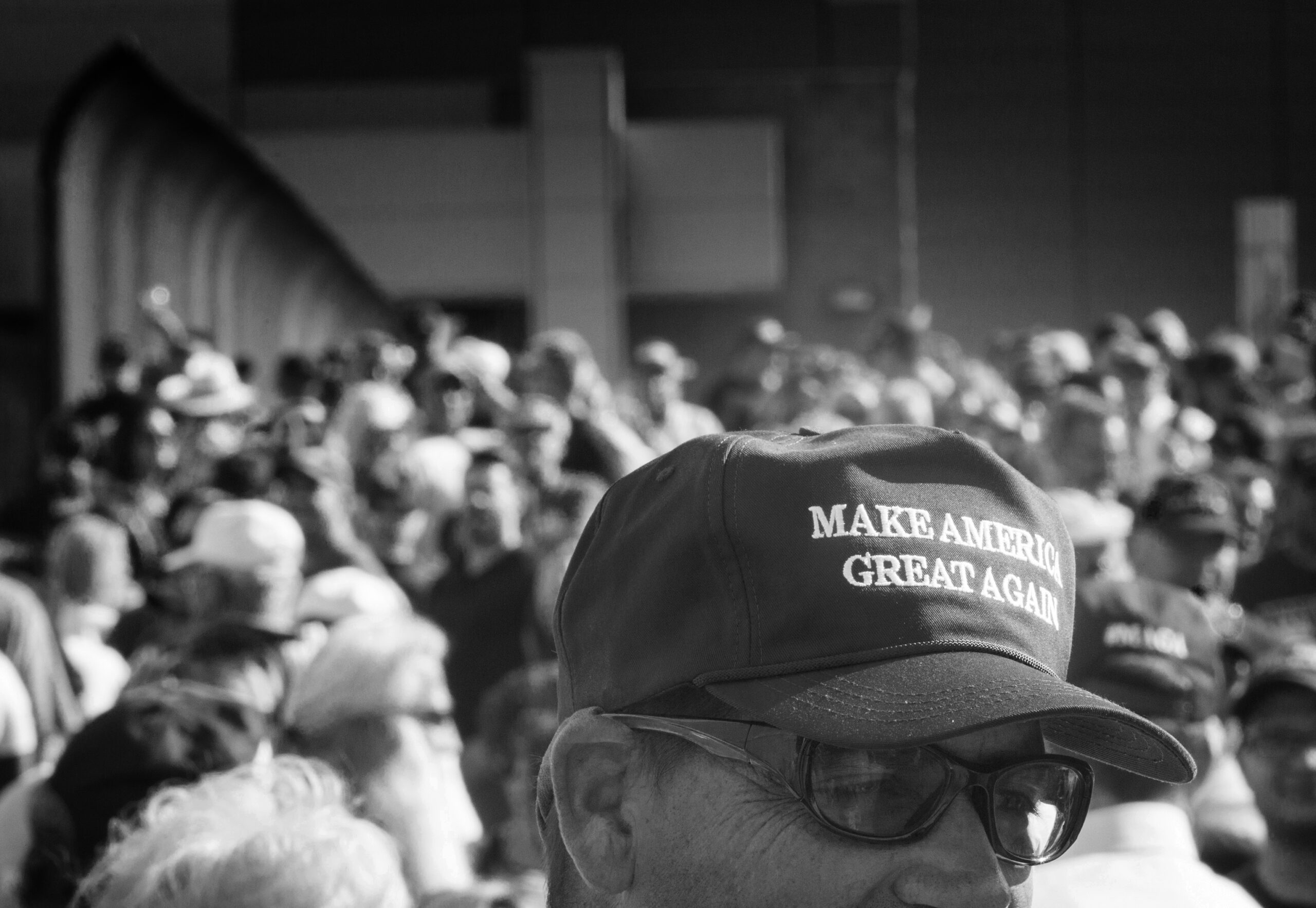 A black and white photo of a man's Make America Great Again hat in front of a crown of people