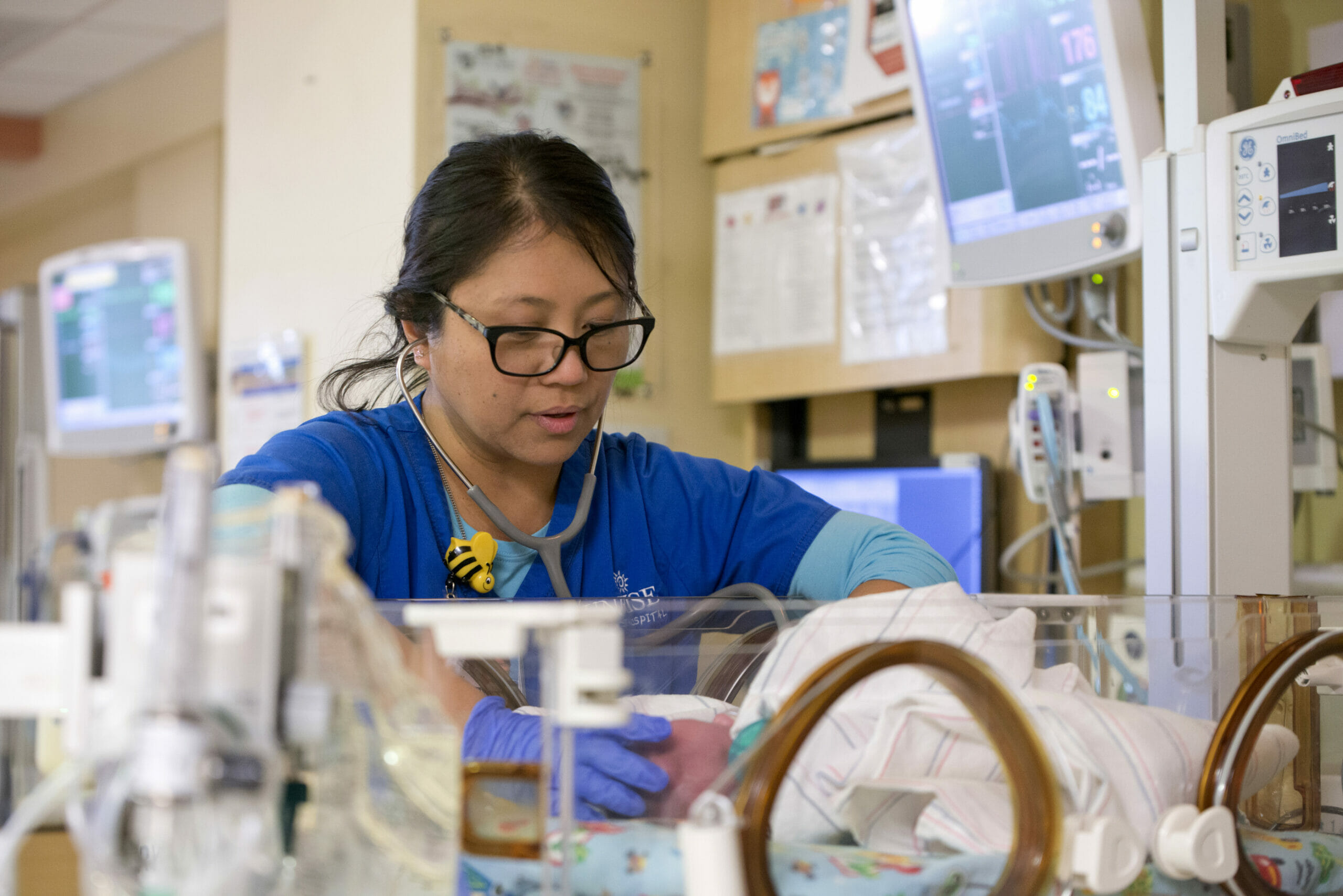 photo of a nurse in blue scrubs leaning over a basinnet