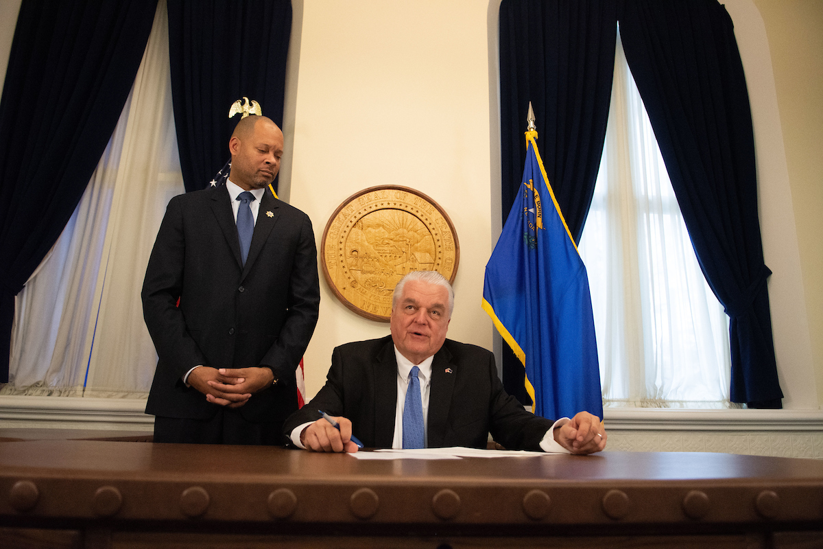 Nevada Governor Steve Sisolak, seated, with Attorney General Aaron Ford, standing, in the Nevada State Capitol