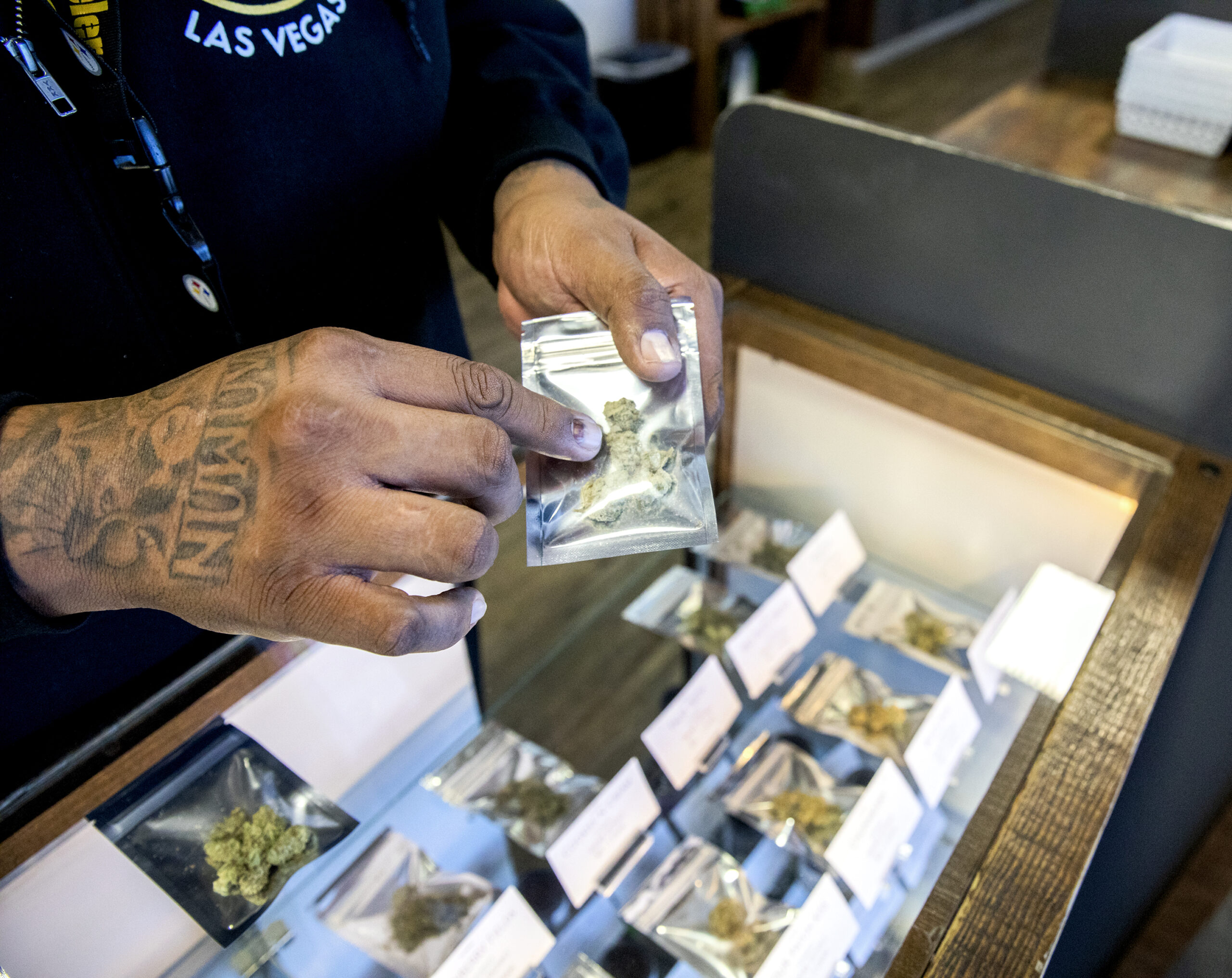 Man's hands holding and showing marijuana products above a sales counter