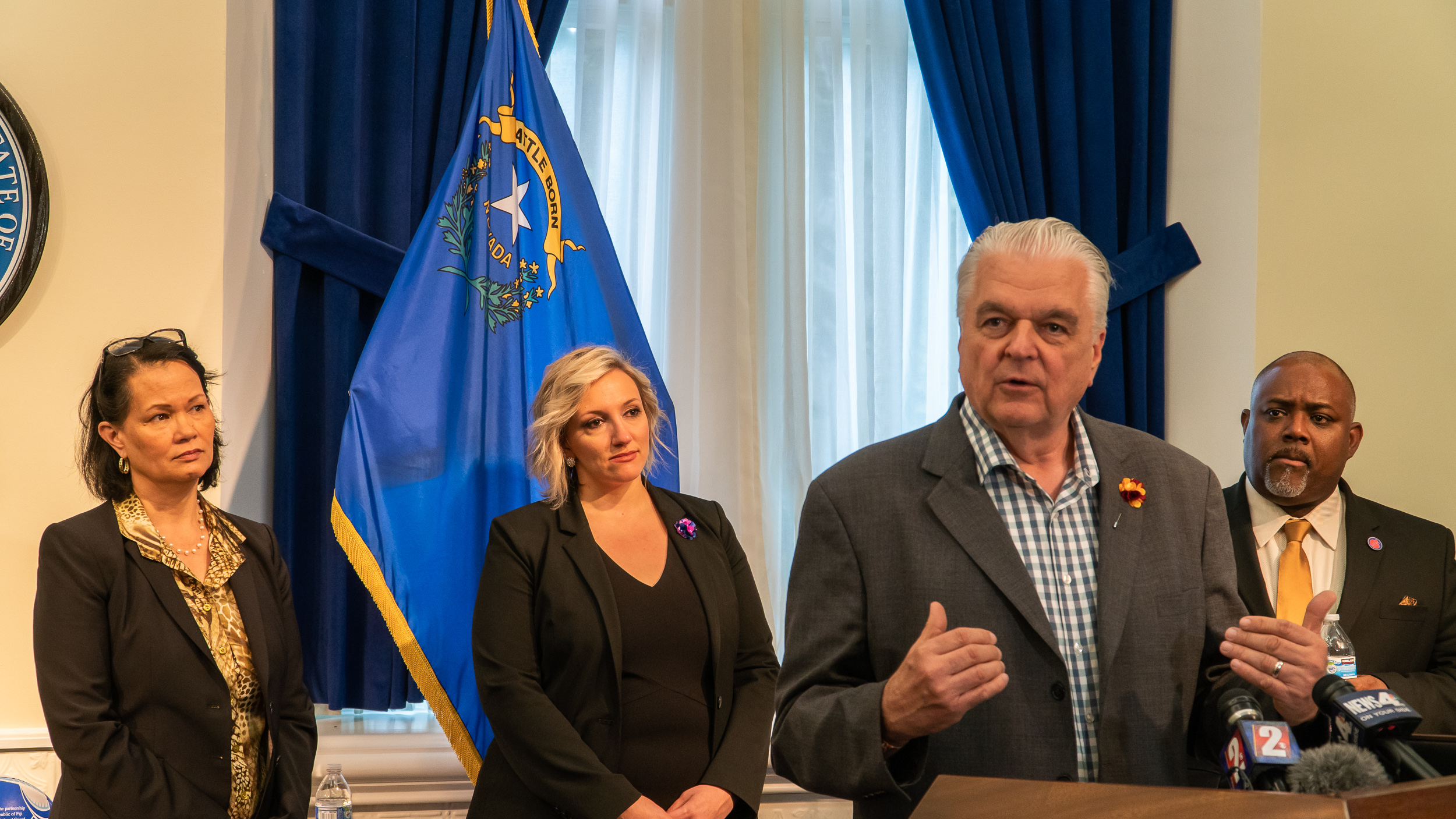 Nevada Governor Steve Sisolak speaking at a podium with Speaker Jason Frierson, Senate Majority Leader Nicole Cannizzaro and Nevada State Superintendent Jhone Eberton standing behind him