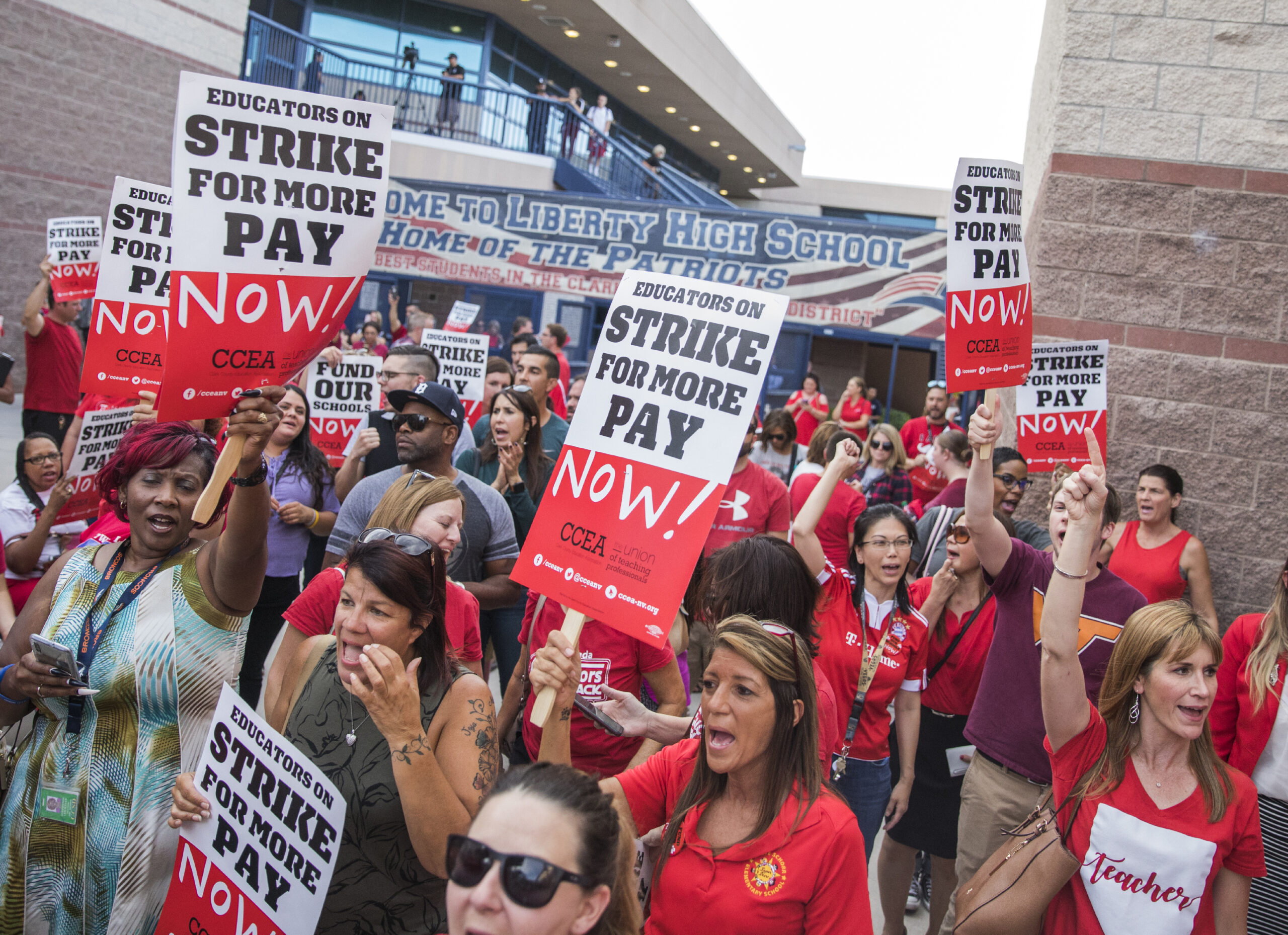 A group of teachers in red shirts with signs at a rally in front of Liberty High School