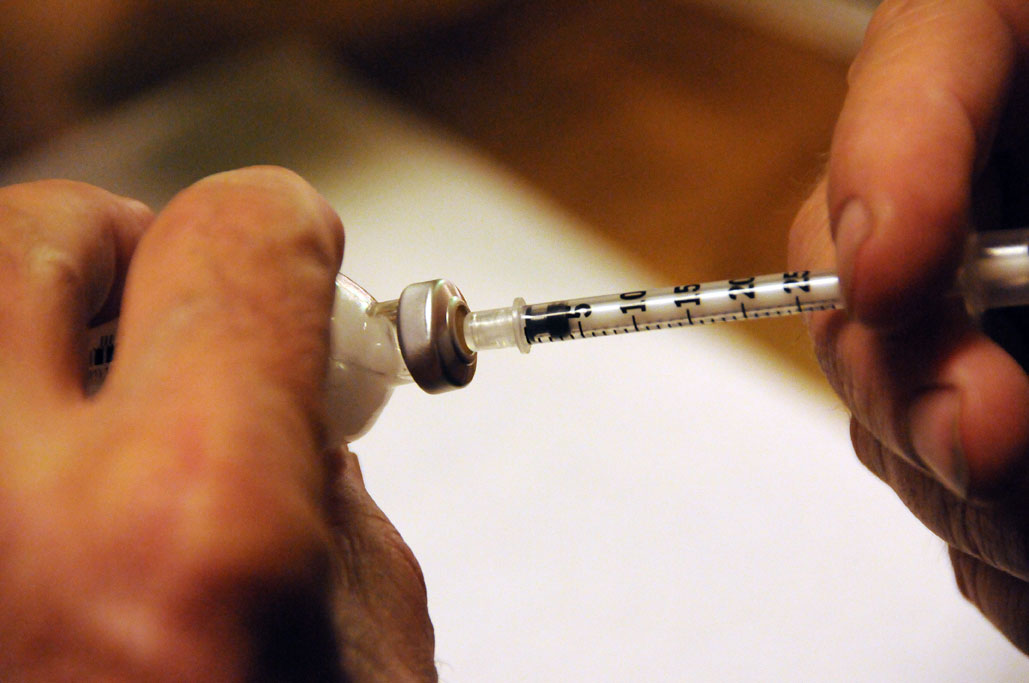 Photo of hands holding a needle inserted into a bottle of insulin