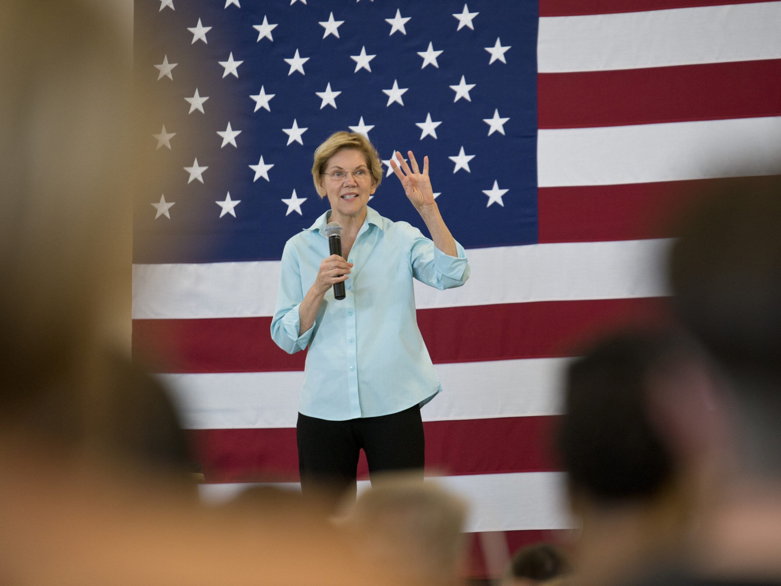 Massachusetts Senator Elizabeth Warren speaking to a crowd while standing in front of an American flag