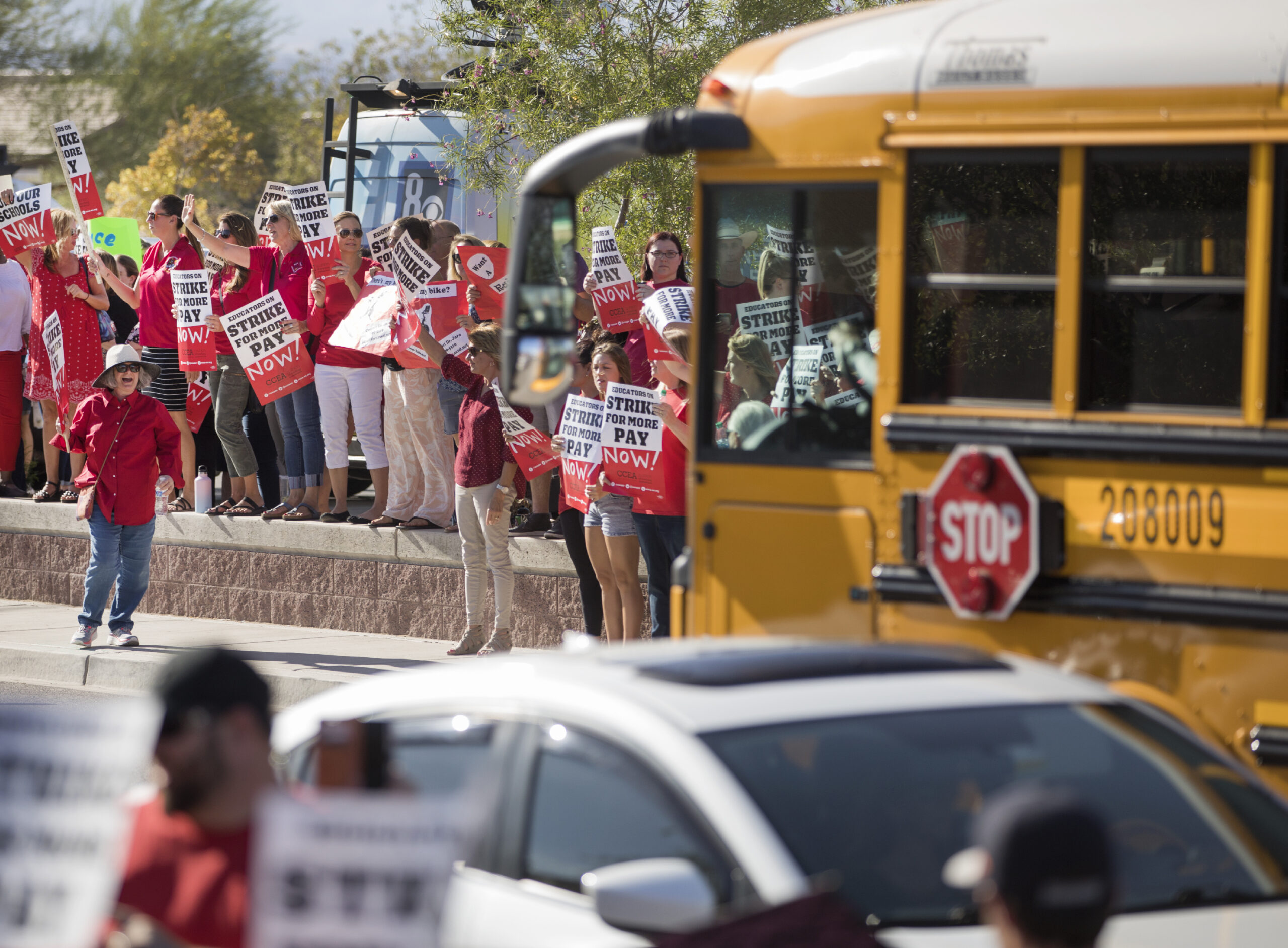 A school bus parked in front of a group of teachers wearing red shirts during a rally