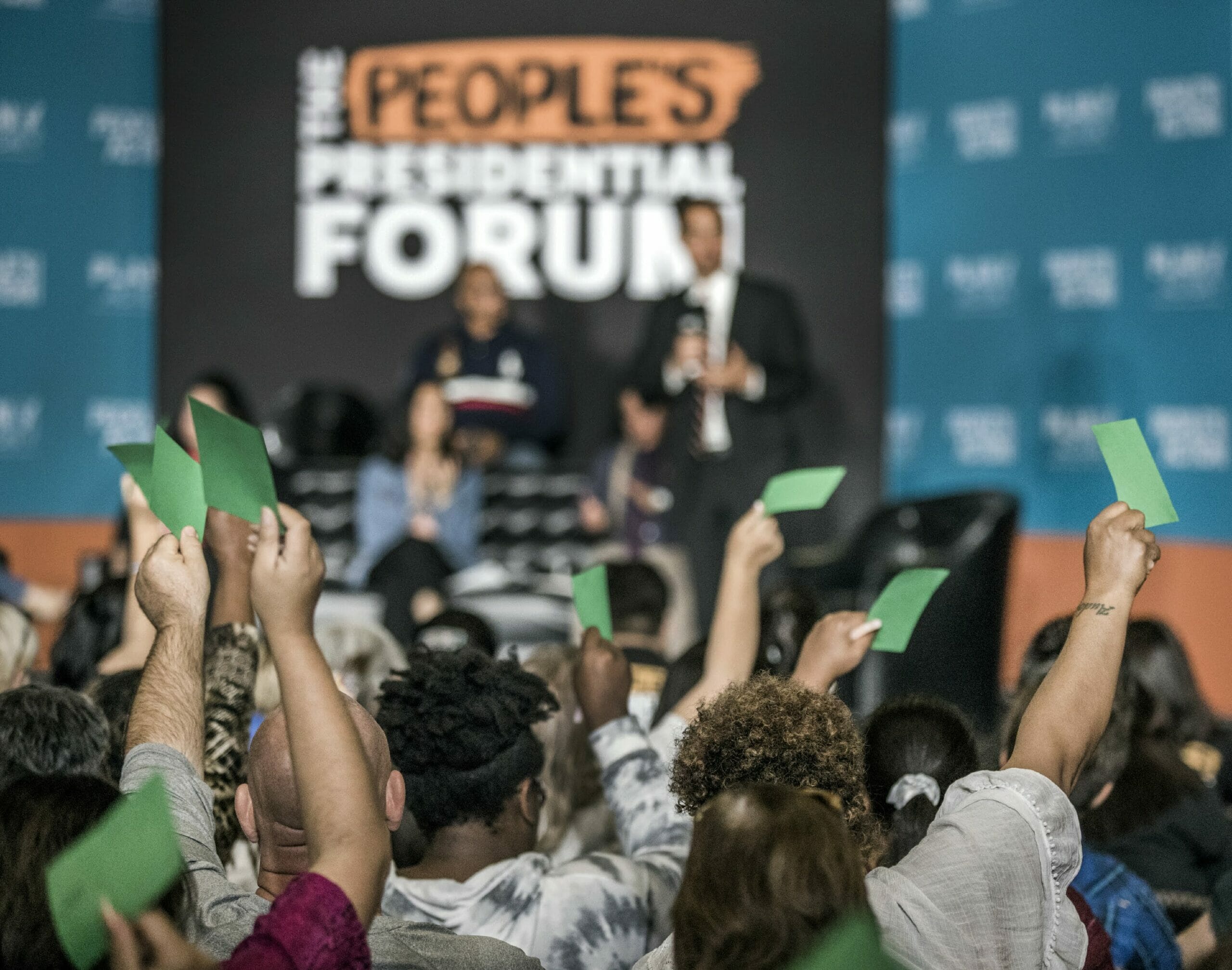 People wave green cards at a presidential forum