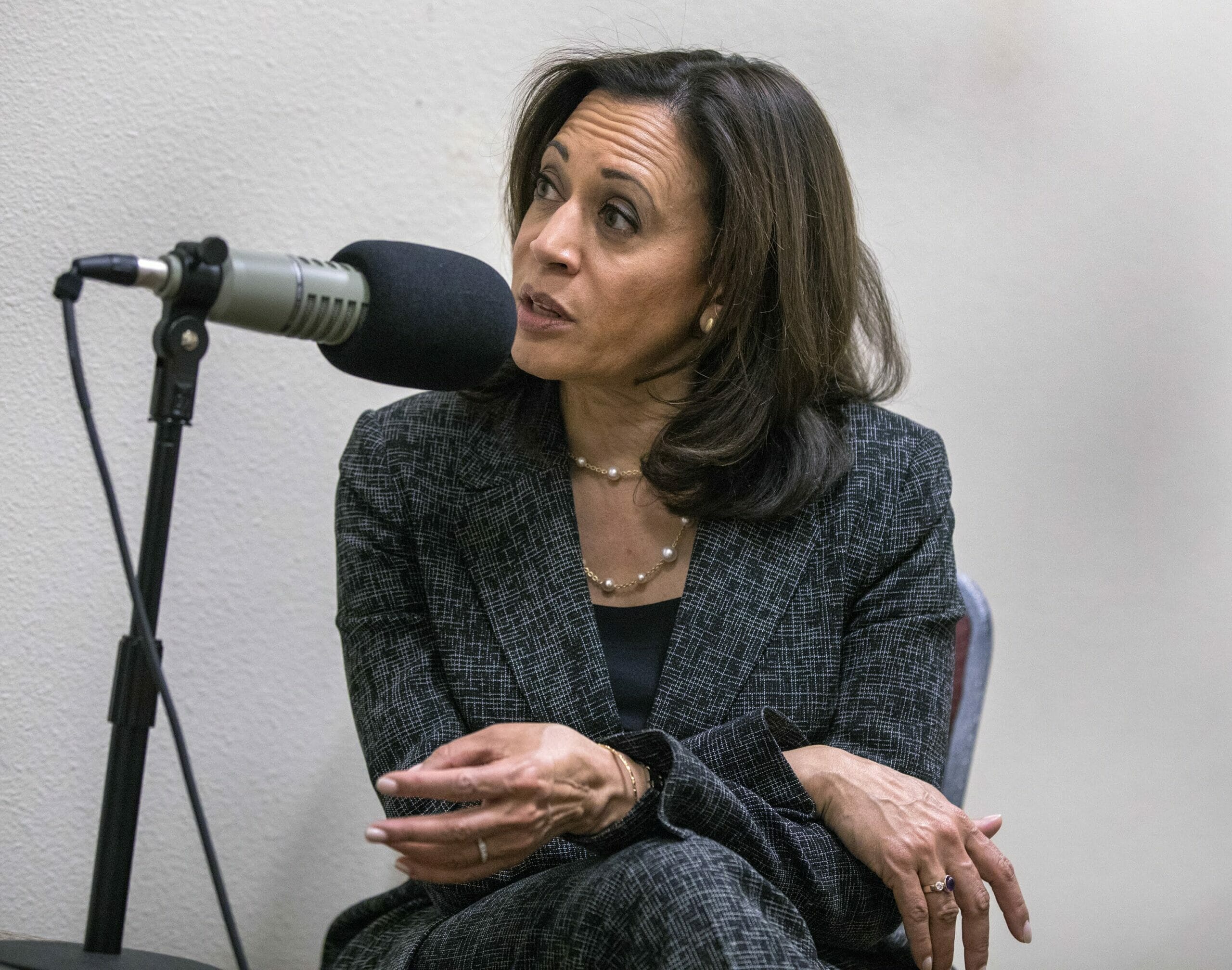 Kamala Harris in a grey suit seated at a microphone