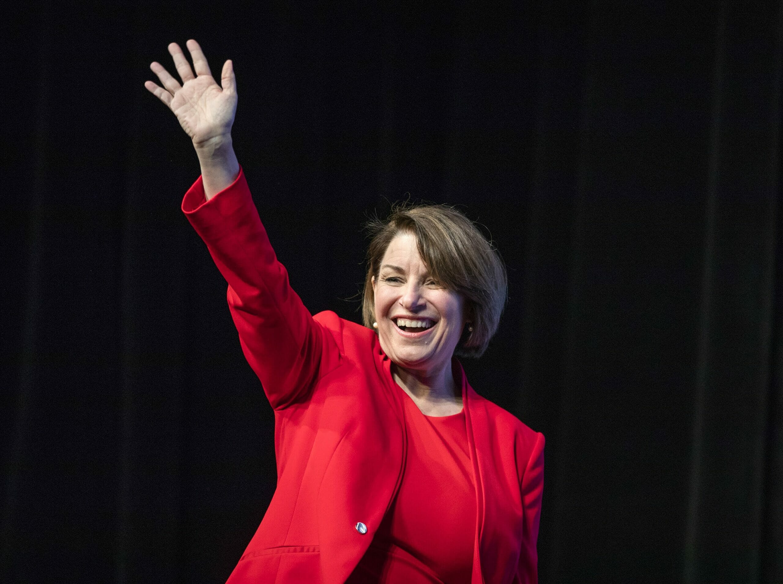 Amy Klobuchar in a red dress suit waiving