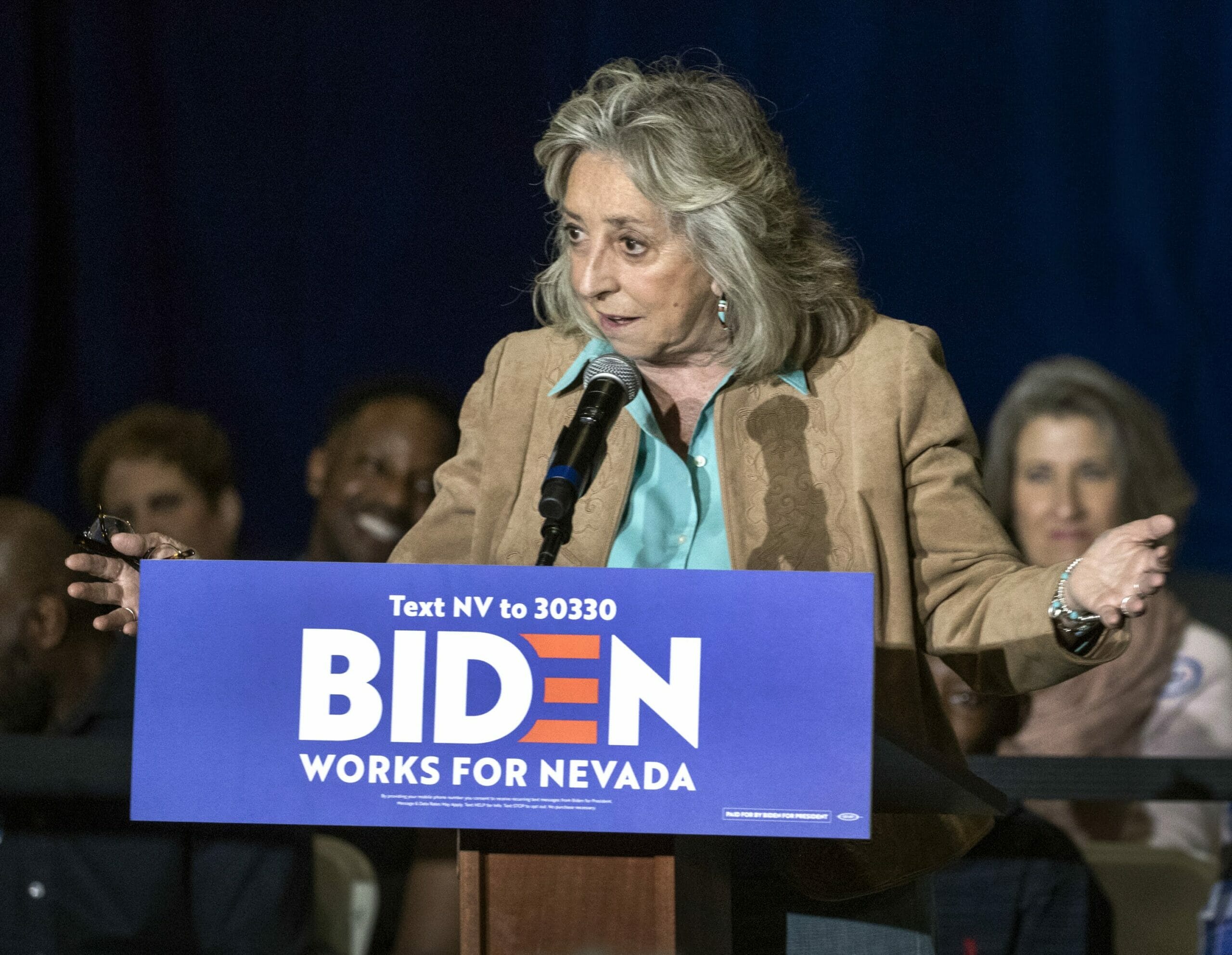 Dina Titus at a podium in a blue shirt and tan jacket