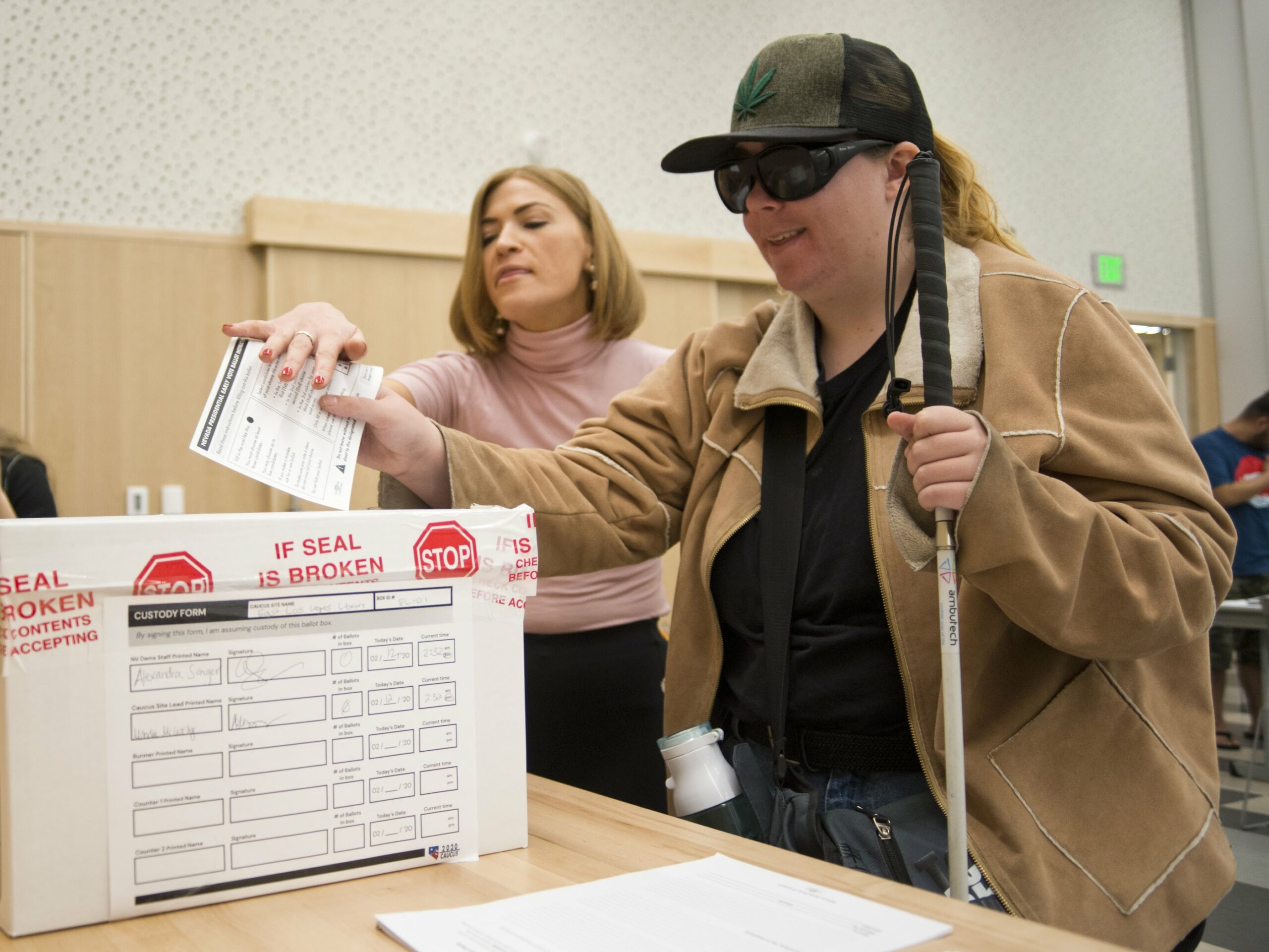 Alyssa Cass, with the Nevada State Democratic Party, left, helps Shannon Bickford, who is blind, through the voting process during the first day of early voting for the Nevada Caucus at the East Las Vegas Library