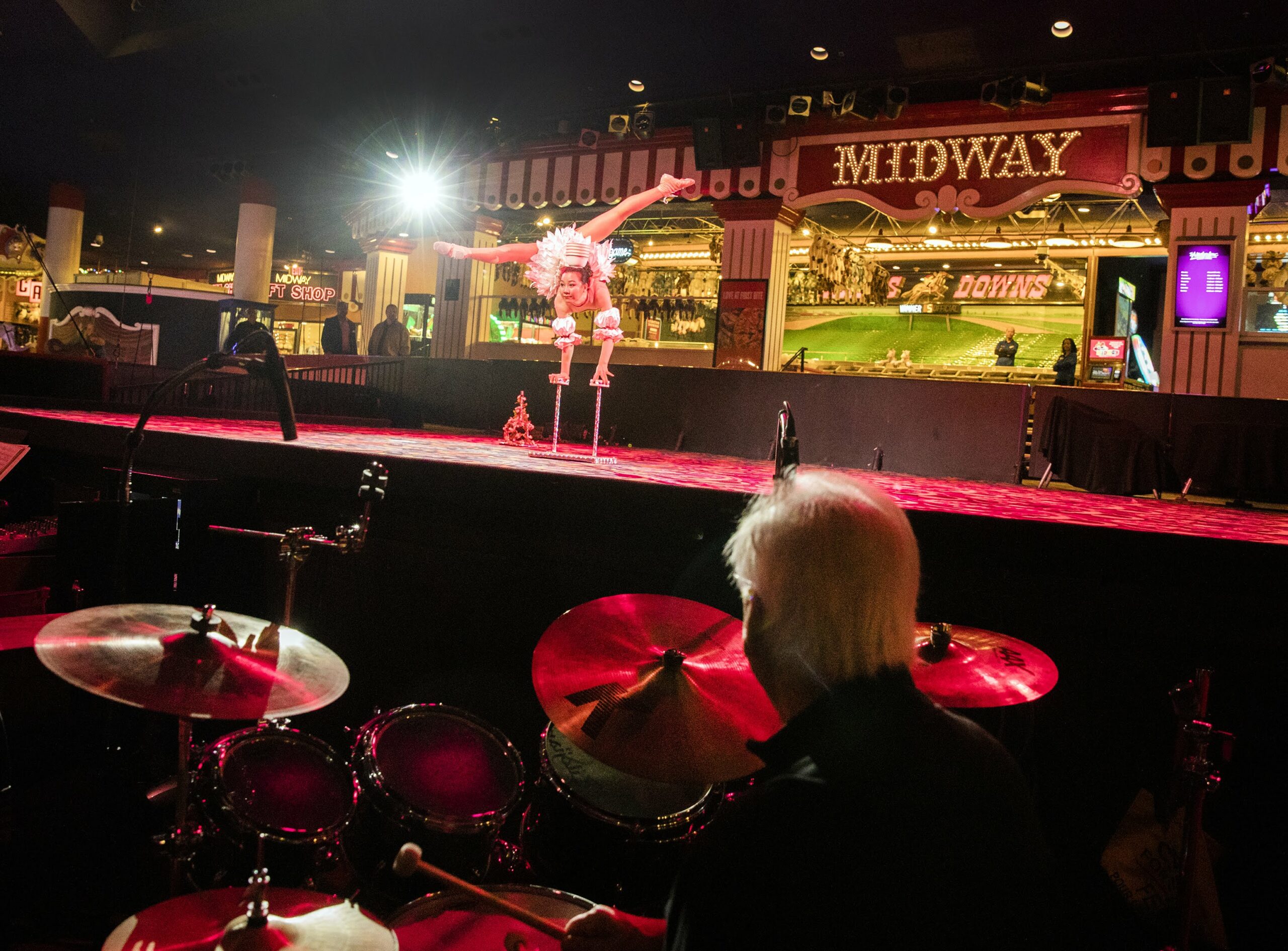 a man drums while an acrobat performs in front of him.