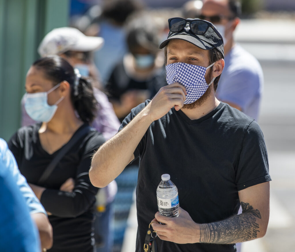 A man pulls at his mask in line