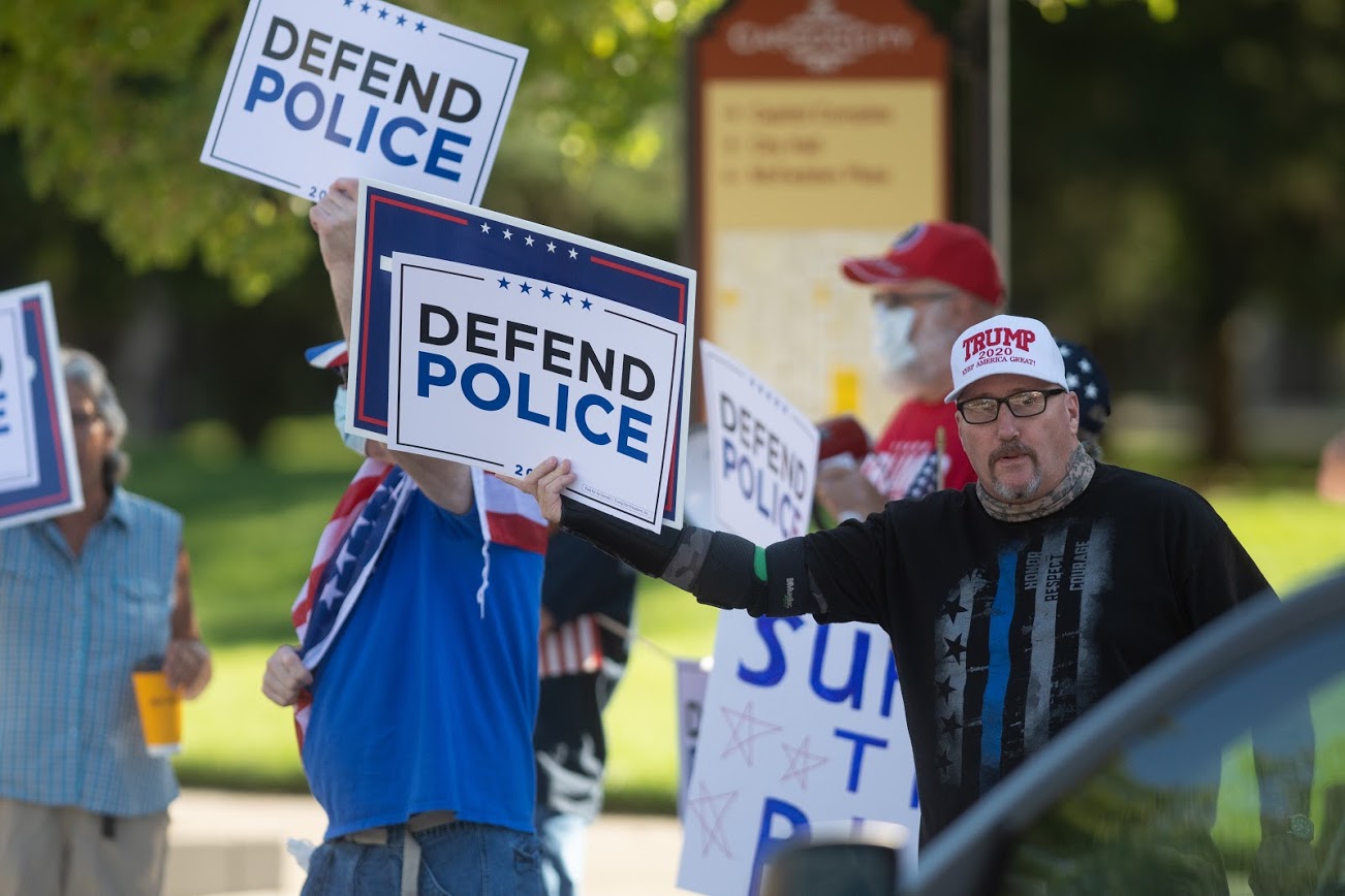 A man wearing a Trump 2020 hat with a sign that says "Defend Police"