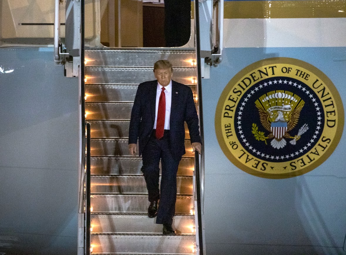 President Trump in a blue suit and red tie coming down the stairs of Air Force One