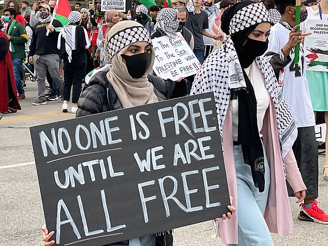 Woman holding "No one is free until we are all free" sign in a crowd.