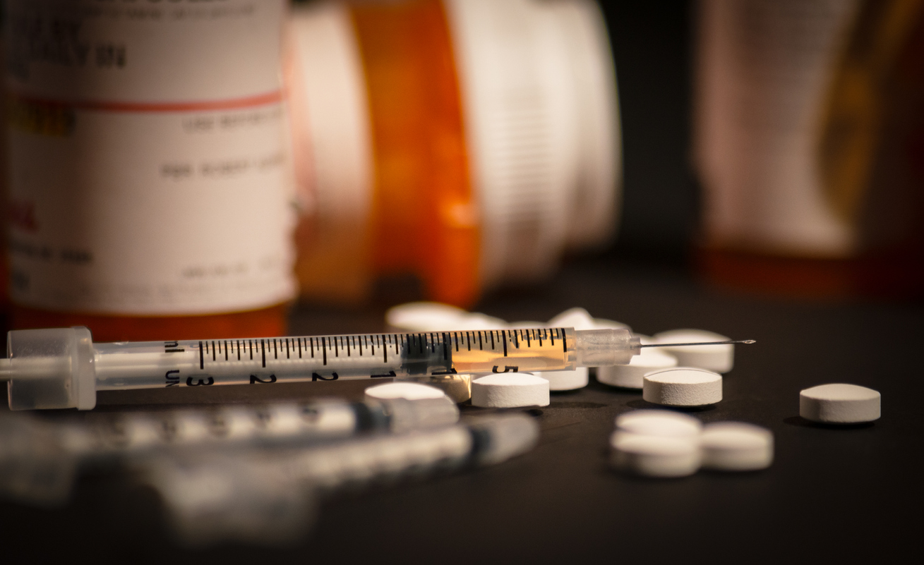 An injectable drug in a syringe with prescription medication strewn about. Photo illustration by Darwin Brandis on iStock.com.