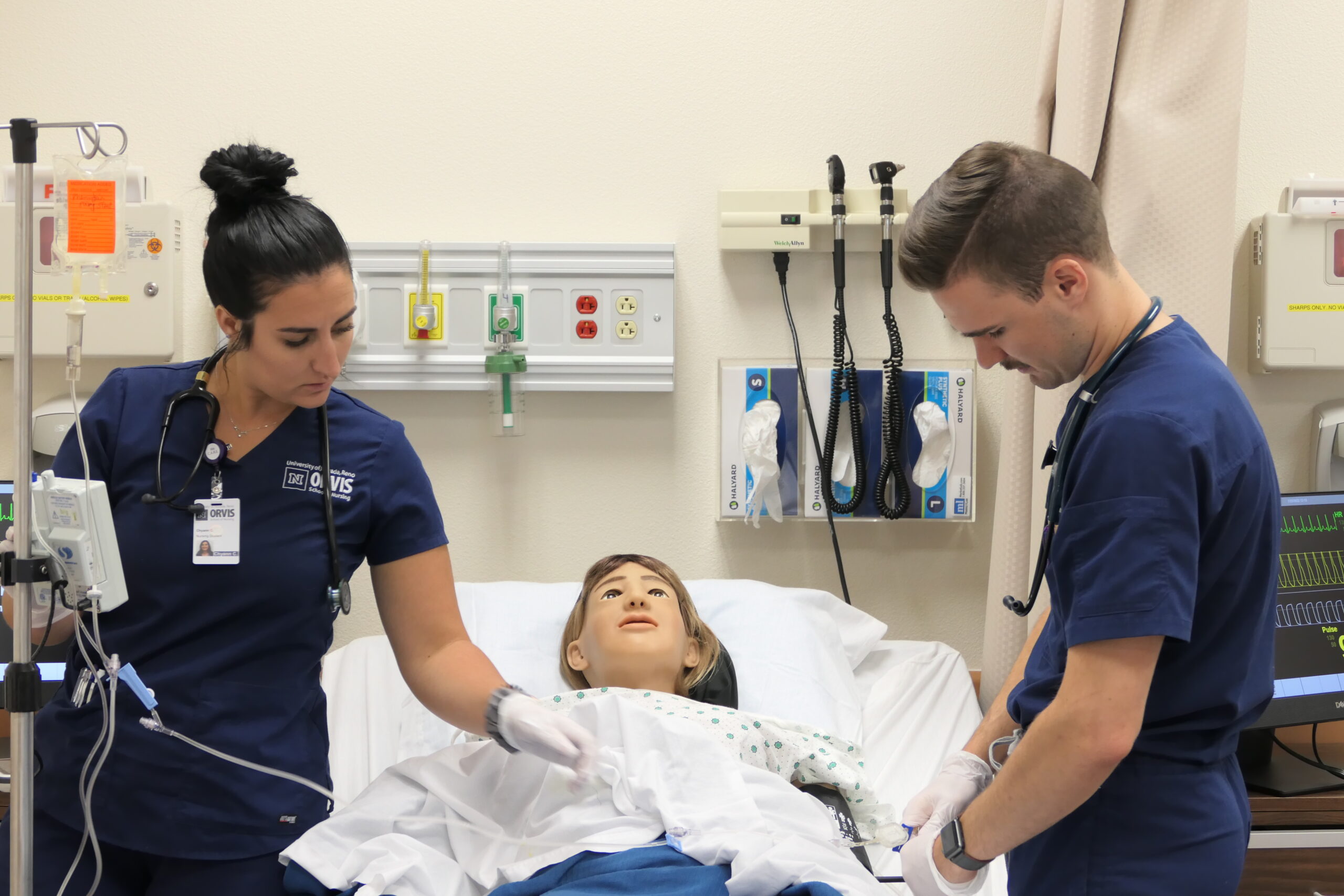 Two nursing students practicing administering medication to a patient dummy.