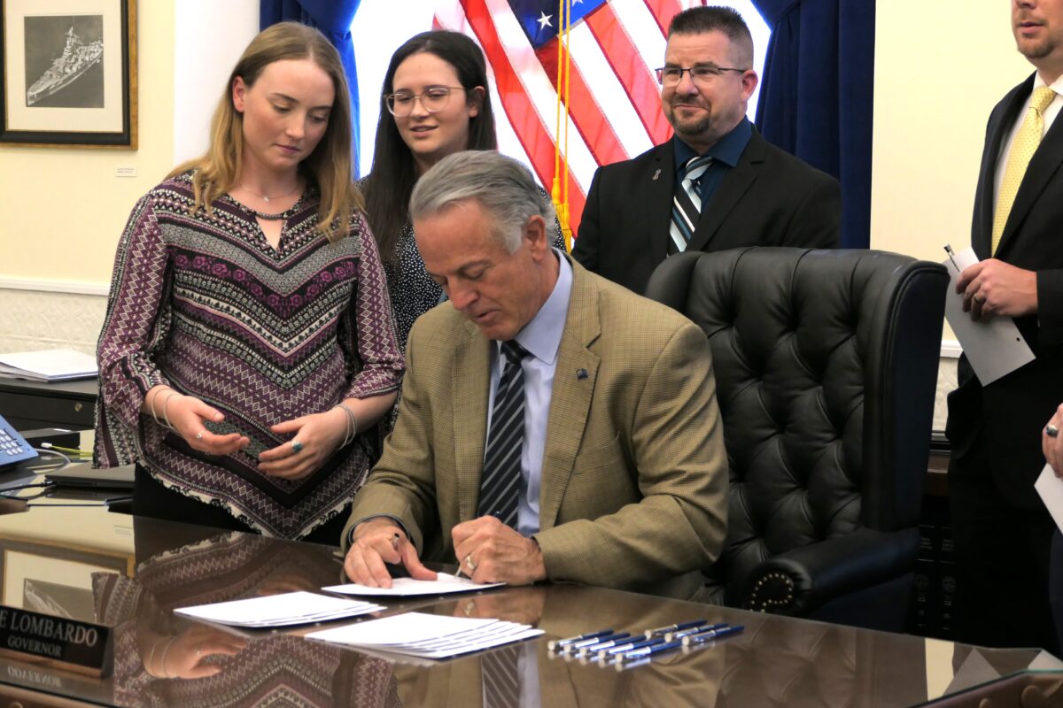 Stella Thornton (left) watches as Gov. Joe Lombardo (seated) signs SB80 during the bill's ceremonial signing in Carson City on Thursday, June 15, 2023. (Carly Sauvageau/The Nevada Independent).