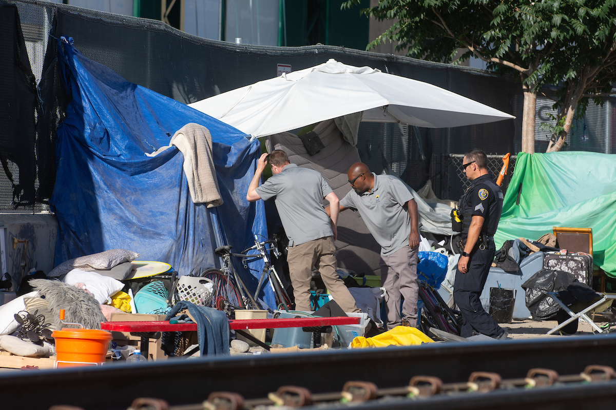 A Reno Police officer and two members of the city's Clean and Safe Field Team during a clean up of a camp along the train tracks between Record Street and the Wells Avenue overpass in Reno on July 18, 2023. (David Calvert/The Nevada Independent)
