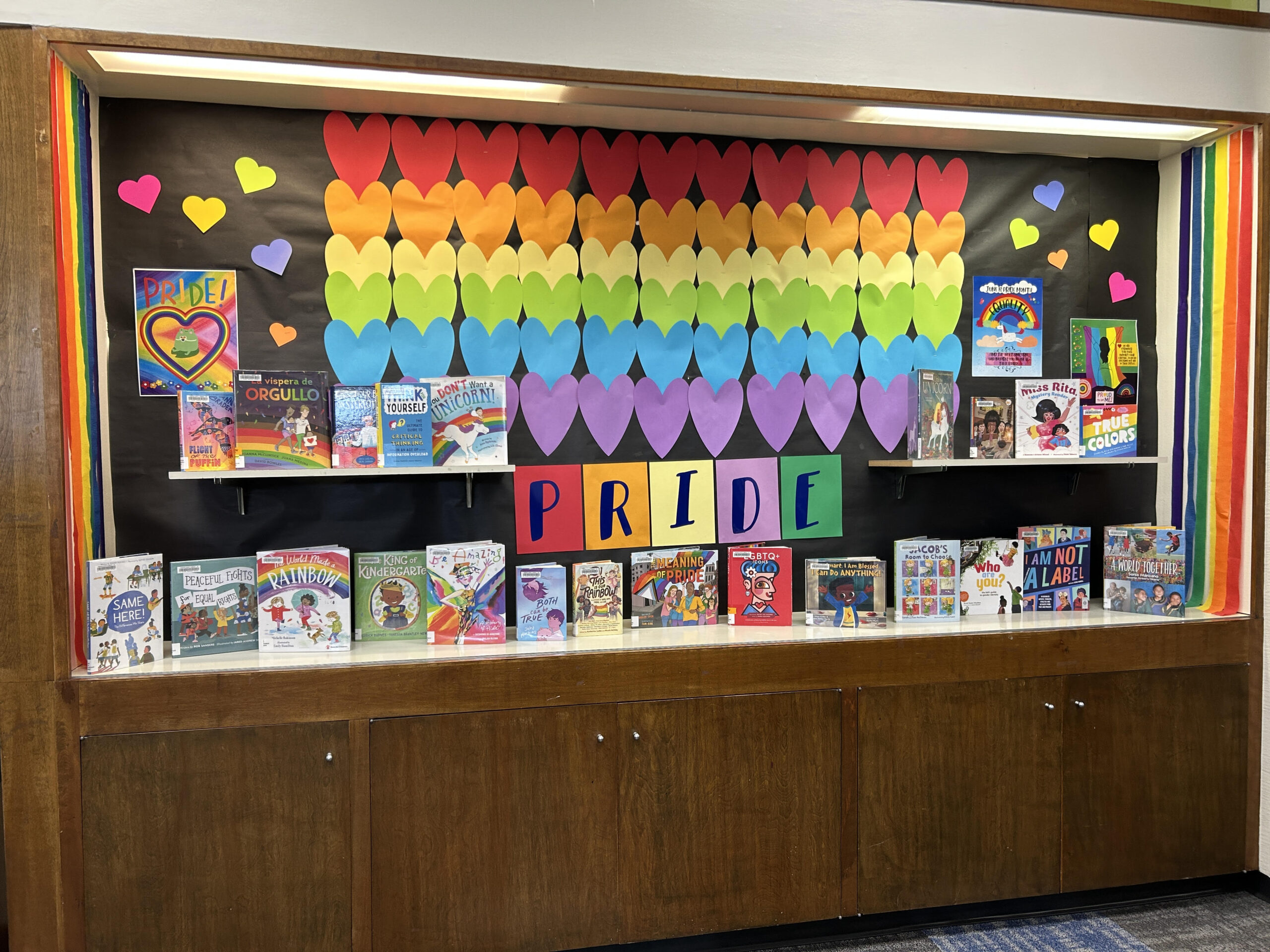 A library display decorated with rainbow paper hearts and pride-themed books.