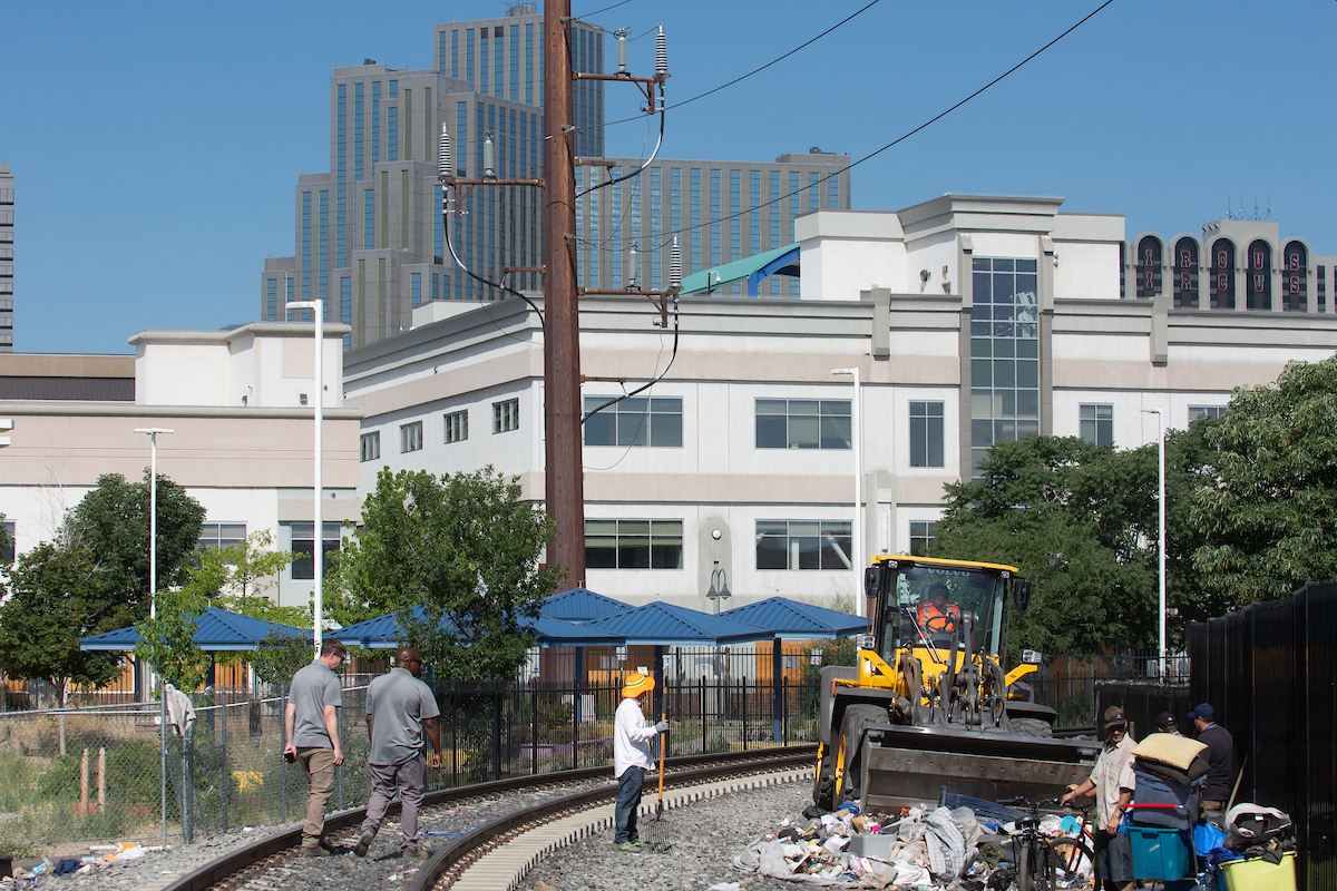 The city of Reno's Clean and Safe Field Team clean up a trash pile during a sweep of a camp along the train tracks between Record Street and the Wells Avenue overpass in Reno on July 18, 2023. (David Calvert/The Nevada Independent)