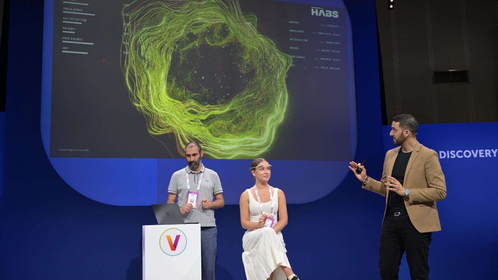 3 people on stage, woman is wearing a brain sensor and the waves are shown in a big screen behind her, one man monitors a computer and one is presenting
