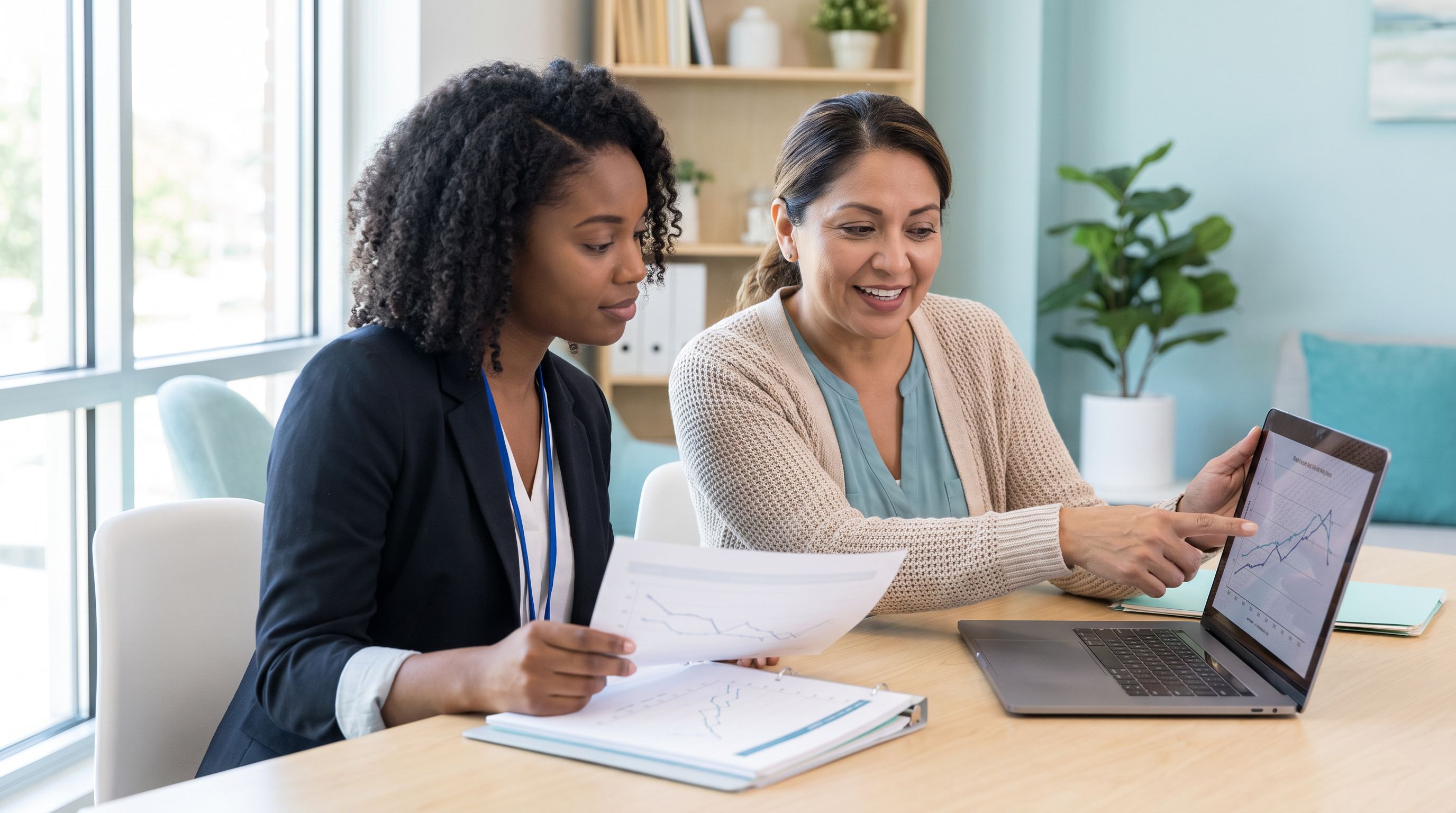 A BCBA fieldwork trainee and her supervisor review printed behavior data graphs together at a desk in a bright modern ABA clinic office.