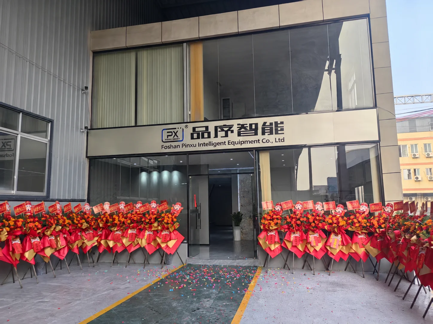 Entrance of Foshan Pinxu Intelligent Equipment Co., Ltd, with the company sign above the glass doors and flower stands outside