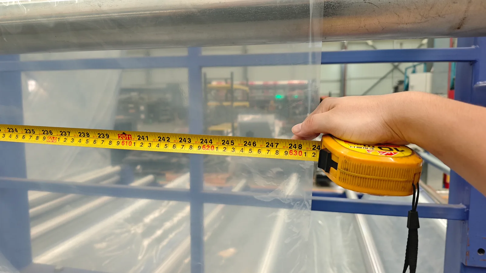 A hand holding a tape measure across clear film to record its dimensions