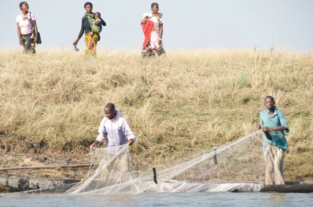 Women head to market, as men pull in nets, Zambia. Photo by Patrick Dugan, 2012.