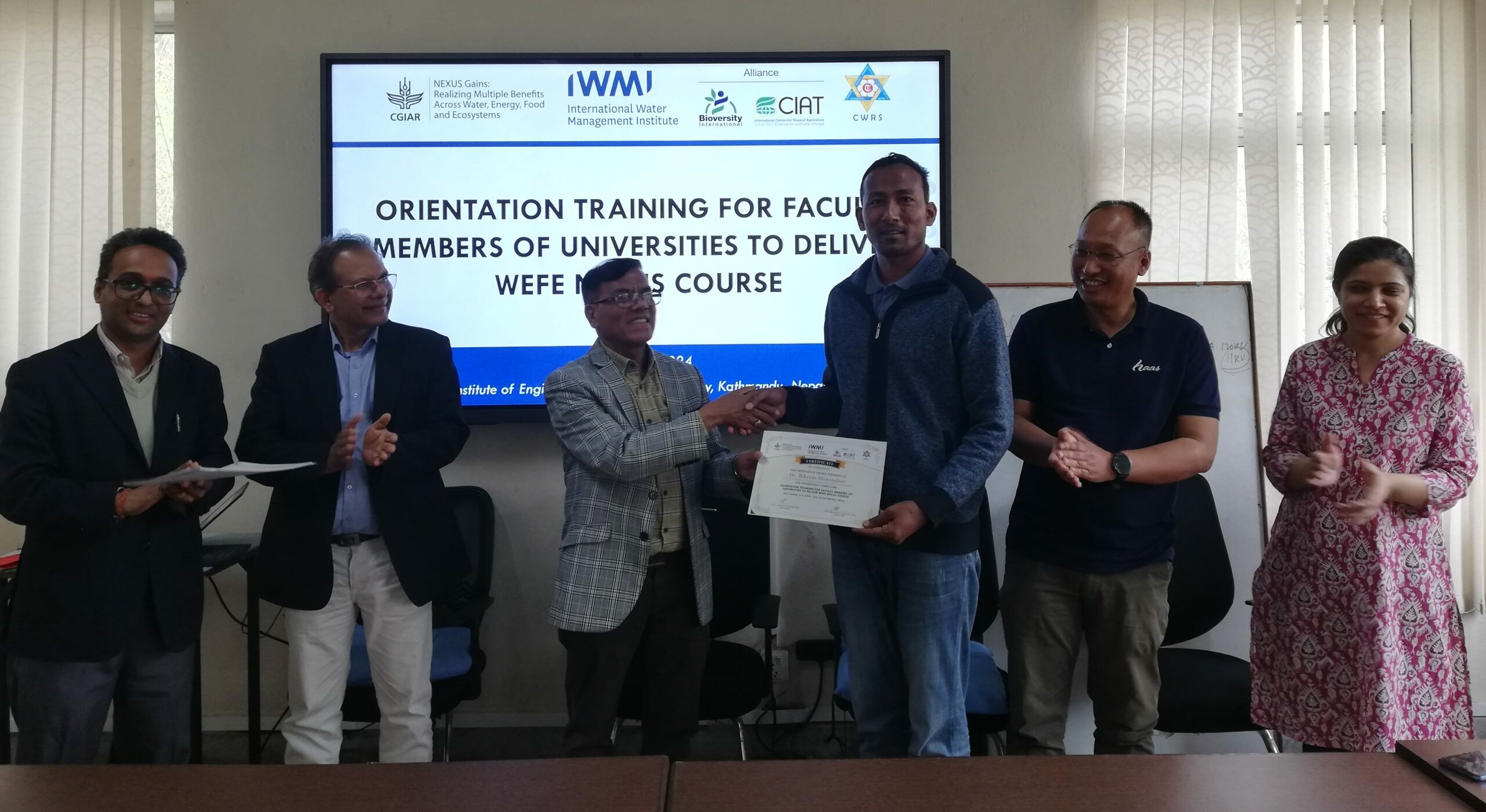 Photo showing people standing in front of a TV screen with the title of a training course